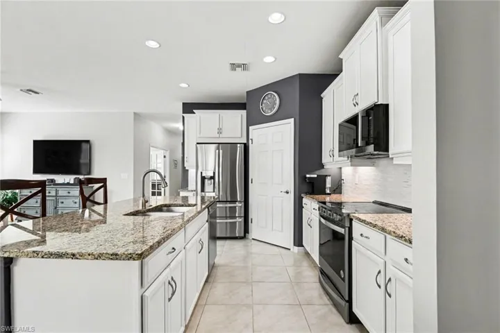 Kitchen featuring stainless steel appliances, light stone countertops, white cabinets, a center island with sink, and recessed lighting