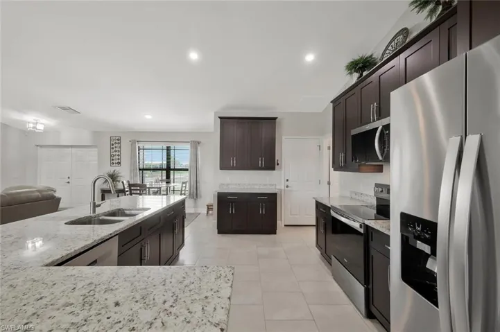 Kitchen with stainless steel appliances, light stone counters, dark wood finish cabinetry, recessed lighting, and light tile patterned floors