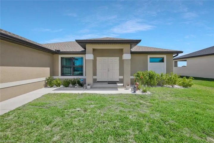 View of exterior entry with a lawn, stucco siding, and roof with shingles