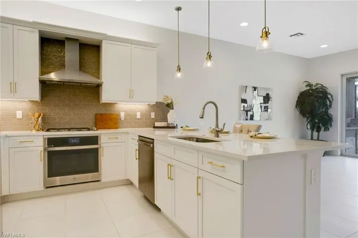 Kitchen featuring light countertops, visible vents, appliances with stainless steel finishes, a sink, and wall chimney range hood