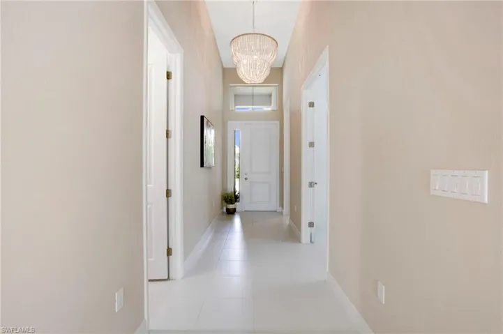 Hallway featuring light tile patterned flooring, baseboards, and an inviting chandelier