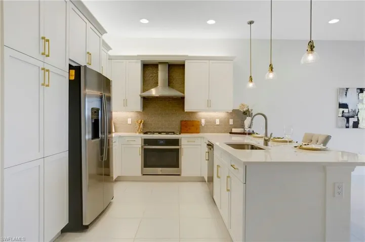 Kitchen with tasteful backsplash, a sink, wall chimney range hood, a peninsula, and appliances with stainless steel finishes