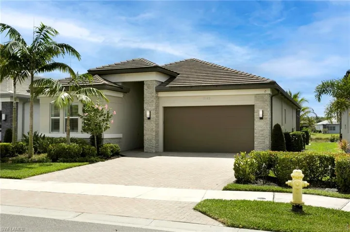 View of front of house with stucco siding, an attached garage, stone siding, a tiled roof, and decorative driveway