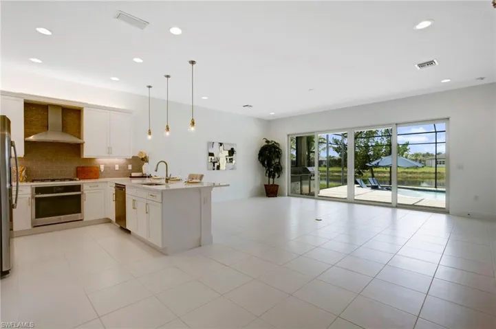 Kitchen featuring visible vents, a peninsula, stainless steel appliances, open floor plan, and wall chimney range hood