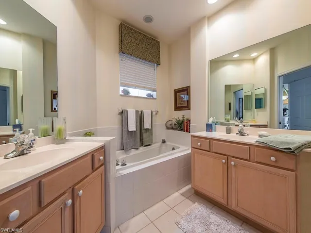 Full bathroom featuring two vanities, a bath, light tile patterned flooring, and recessed lighting