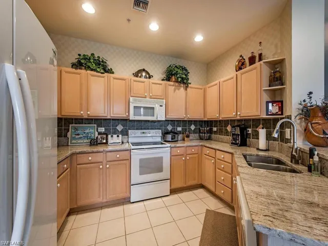 Kitchen with white appliances, open shelves, light stone counters, decorative backsplash, and wallpapered walls