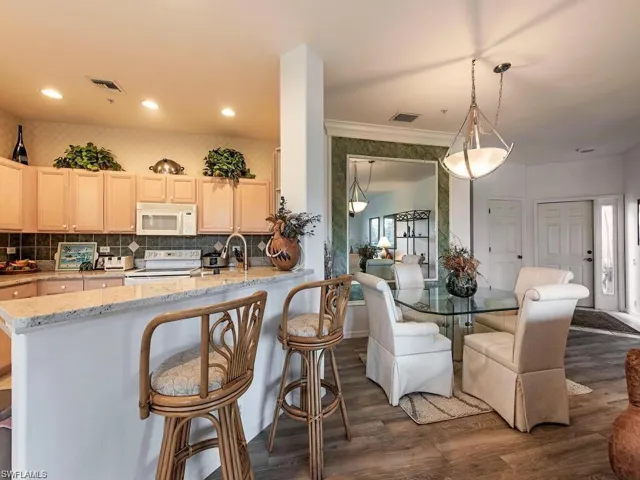 Kitchen with light wood finish cabinetry, light stone counters, white appliances, dark wood-style flooring, and a breakfast bar area