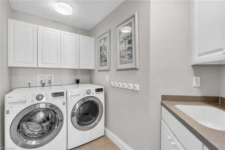 Laundry room featuring light tile patterned floors, cabinets, sink, and independent washer and dryer
