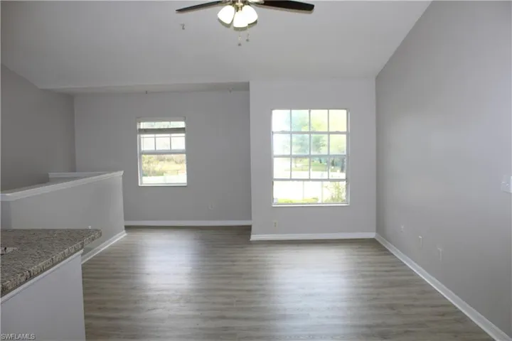 Unfurnished room with ceiling fan, plenty of natural light, baseboards, and wood finished floors