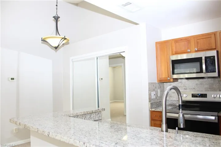Kitchen featuring decorative light fixtures, light stone countertops, stainless steel appliances, and tasteful backsplash