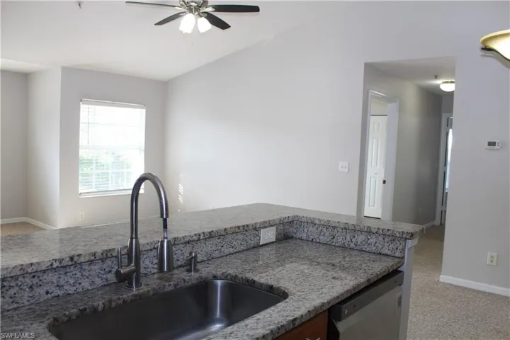 Kitchen with stainless steel dishwasher, light colored carpet, ceiling fan, and sink
