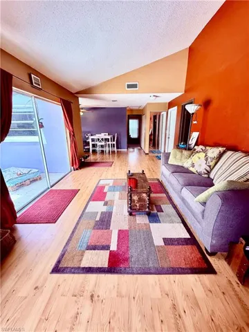 Living room with vaulted ceiling, a textured ceiling, and wood finished floors