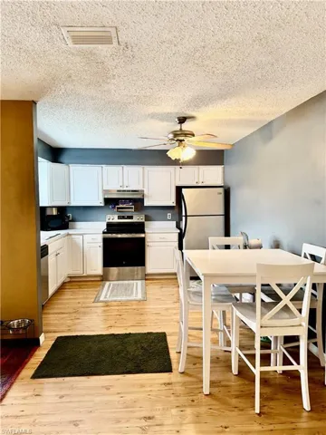 Kitchen with electric stove, freestanding refrigerator, white cabinets, ceiling fan, and a textured ceiling