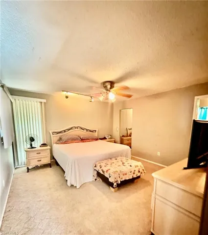 Bedroom featuring a textured ceiling, light colored carpet, ceiling fan, and track lighting