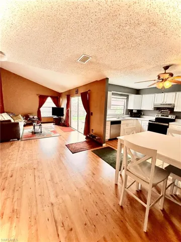 Dining area featuring light wood-style floors, a ceiling fan, lofted ceiling, and a textured ceiling