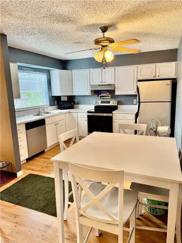 Kitchen with light wood-type flooring, appliances with stainless steel finishes, white cabinets, light countertops, and a textured ceiling