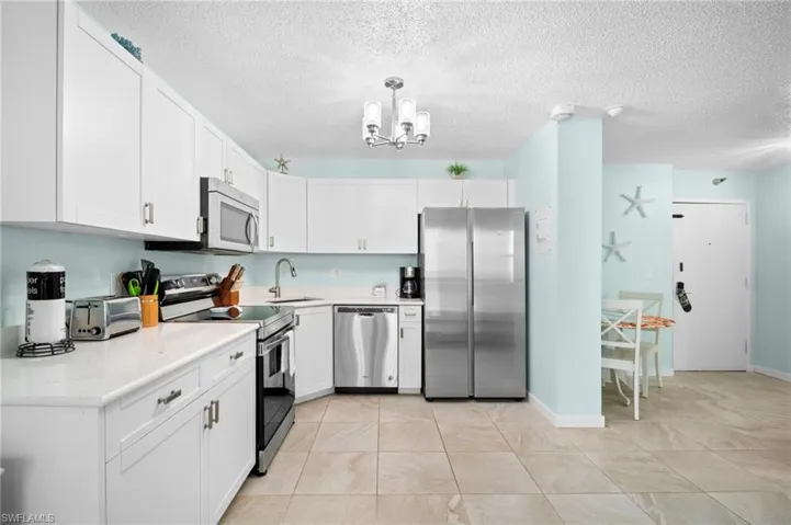 Kitchen featuring stainless steel appliances, white cabinets, a textured ceiling, a chandelier, and pendant lighting