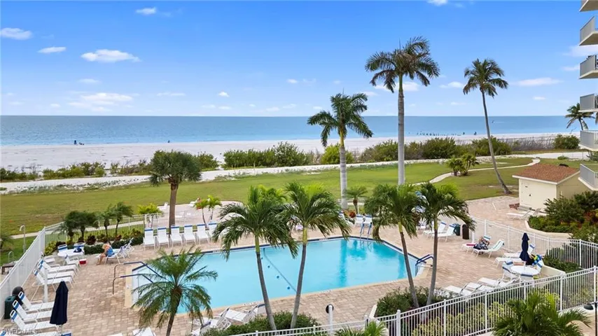 Community pool with a patio area and view of water and beach