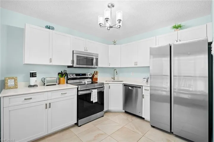 Kitchen featuring appliances with stainless steel finishes, a textured ceiling, pendant lighting, white cabinets, and a chandelier