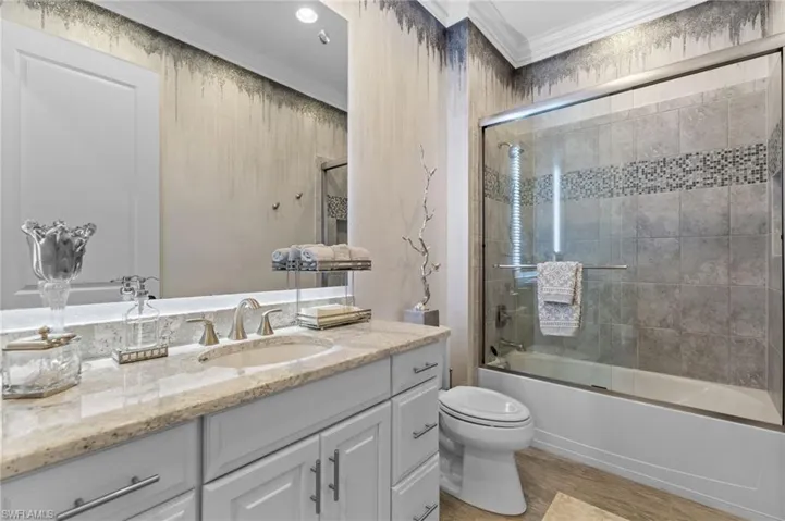 Bathroom with vanity, combined bath / shower with glass door, crown molding, and light wood-style floors