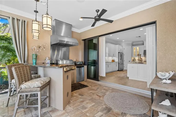 Kitchen with hanging light fixtures, a breakfast bar area, crown molding, stone finish flooring, and dark stone counters