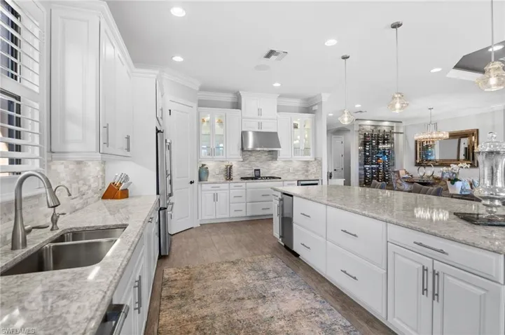 Kitchen with white cabinetry, ornamental molding, dark wood finished floors, light stone counters, and a chandelier