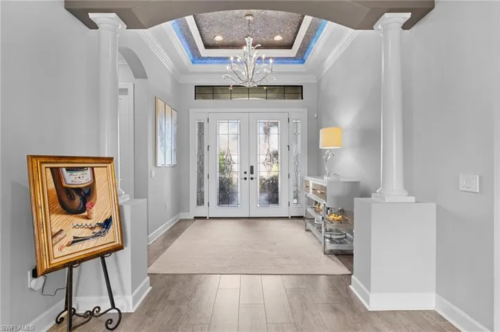 Foyer with crown molding, french doors, suspended lighting, light wood-style flooring, and arched walkways