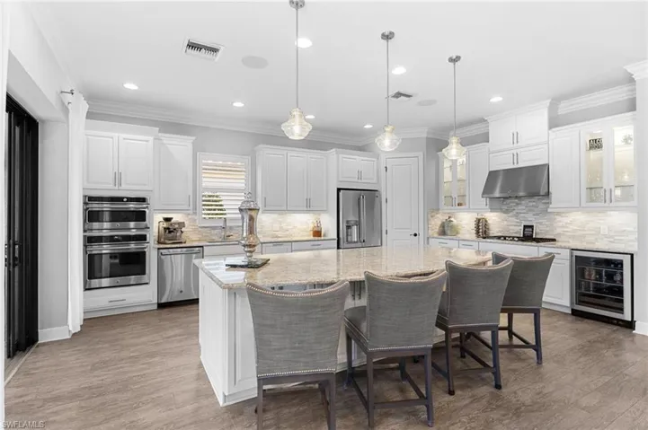 Kitchen featuring ornamental molding, decorative light fixtures, a kitchen breakfast bar, wine cooler, and white cabinetry