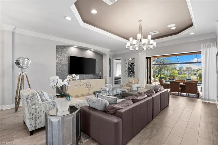 Living area with ornamental molding, wood finished floors, a chandelier, a tray ceiling, and a sunroom