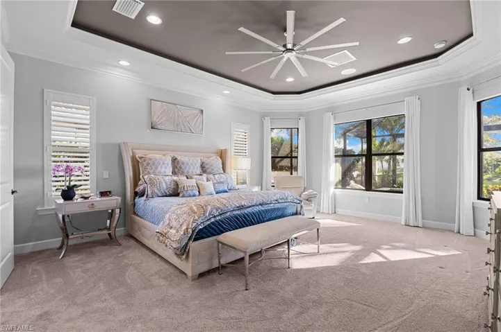 Bedroom with ornamental molding, a raised ceiling, a ceiling fan, and light colored carpet