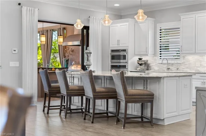 Kitchen with white cabinetry, light stone counters, ornamental molding, decorative light fixtures, and a kitchen bar