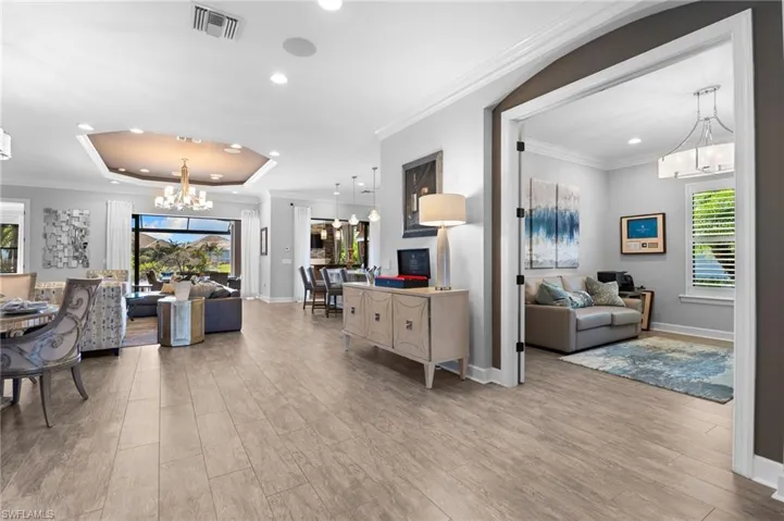 Living area with a chandelier, ornamental molding, light wood finished floors, plenty of natural light, and a raised ceiling