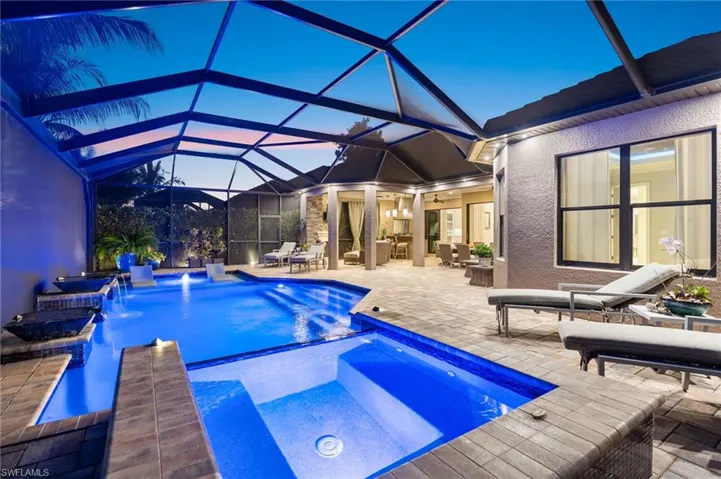 Pool at dusk with a patio, glass enclosure, outdoor dining area, a sunroom, and a pool with connected hot tub