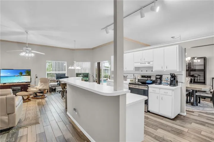 Kitchen with white cabinetry, track lighting, ceiling fan with notable chandelier, and stainless steel range with electric stovetop