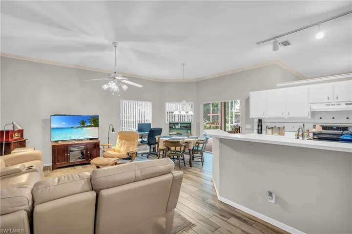 Living room with ceiling fan with notable chandelier, rail lighting, ornamental molding, sink, and light hardwood / wood-style floors