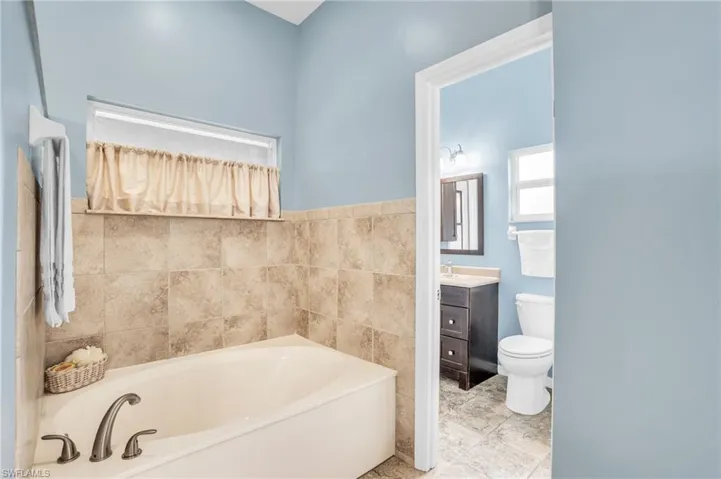 Bathroom with tile patterned flooring, toilet, vanity, tile walls, and a tub