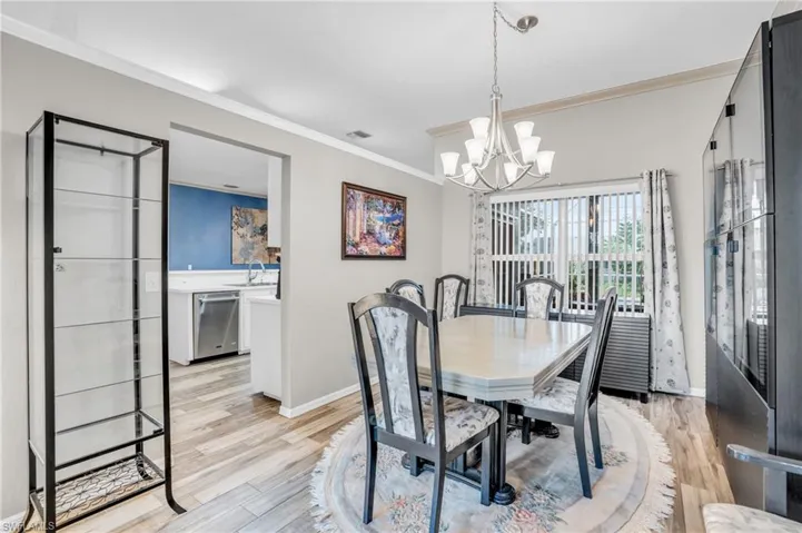 Dining room with crown molding, sink, light wood-type flooring, and an inviting chandelier