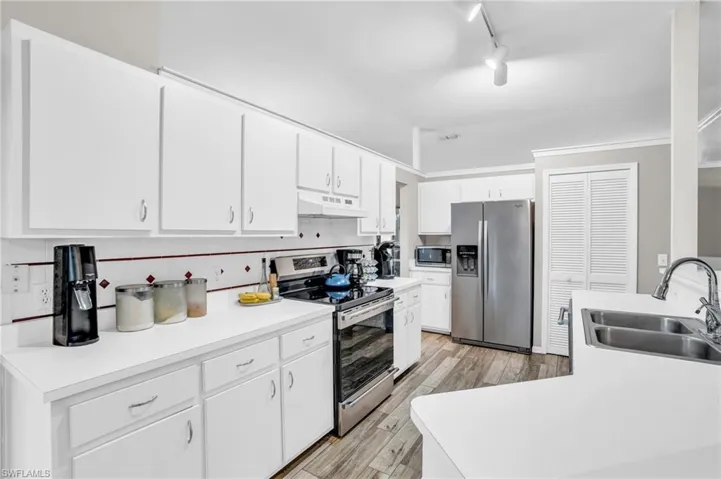 Kitchen featuring appliances with stainless steel finishes, white cabinets, rail lighting, and sink