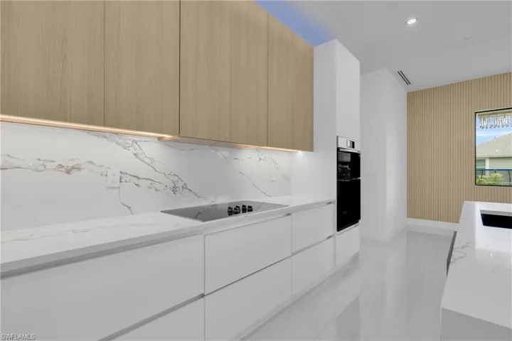 Kitchen featuring modern cabinets, light stone counters, black electric stovetop, tasteful backsplash, and recessed lighting