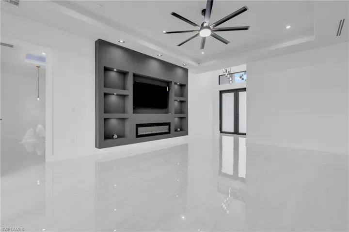 Unfurnished living room with a glass covered fireplace, a tray ceiling, tile patterned floors, recessed lighting, and a ceiling fan