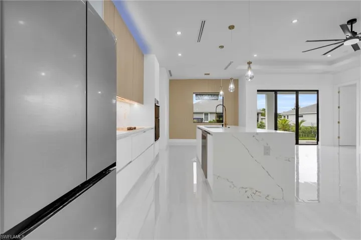 Kitchen featuring freestanding refrigerator, decorative light fixtures, modern cabinets, a center island with sink, and light stone countertops
