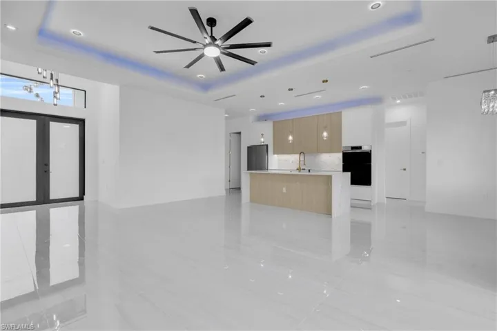 Unfurnished living room featuring a raised ceiling, french doors, recessed lighting, a chandelier, and ceiling fan