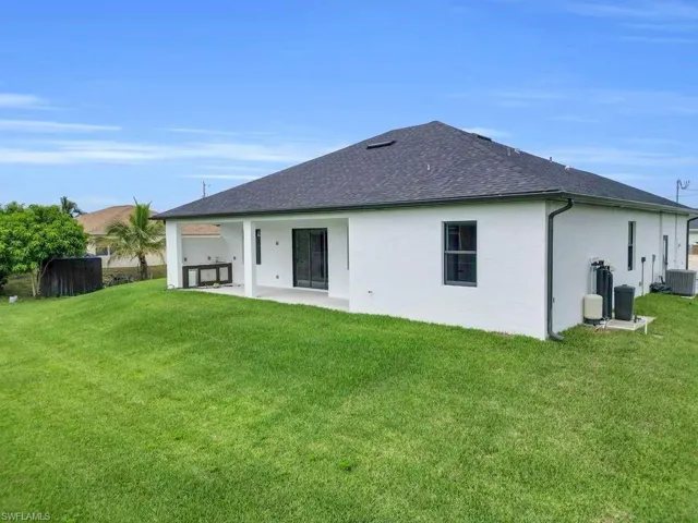 Rear view of house featuring a patio area, a yard, roof with shingles, and stucco siding