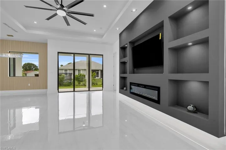 Unfurnished living room with a glass covered fireplace, recessed lighting, built in shelves, a tray ceiling, and tile patterned flooring