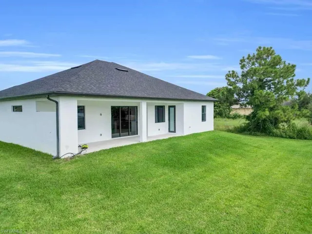 Back of house with stucco siding, a shingled roof, a patio, and a lawn