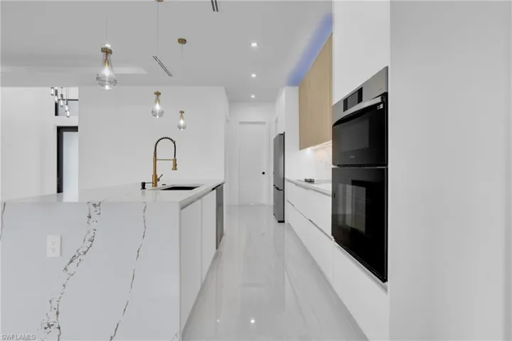 Kitchen with modern cabinets, hanging light fixtures, recessed lighting, light stone counters, and light brown cabinets