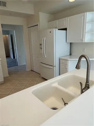 Kitchen with light countertops, white cabinets, newer appliances, light tile patterned floors
