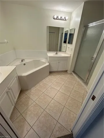 Full bathroom with two vanities, a bath, a stall shower, and light tile patterned floors
