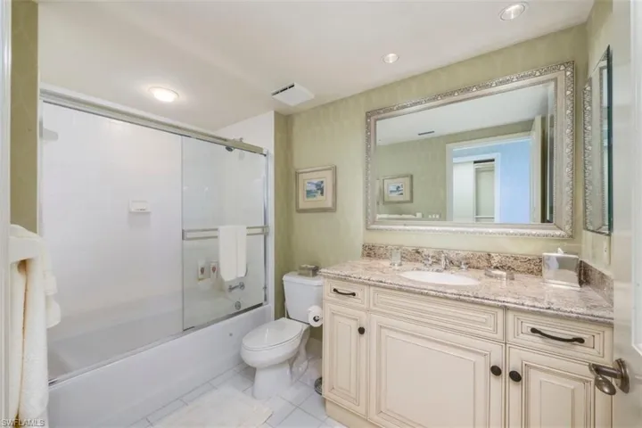 Bathroom with enclosed tub / shower combo, vanity, light tile patterned floors, and recessed lighting