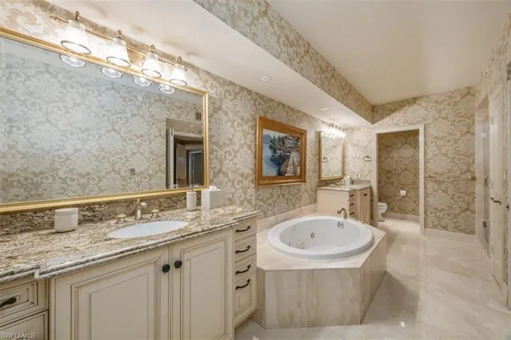 Full bathroom featuring wallpapered walls, vanity, and a tub with jets